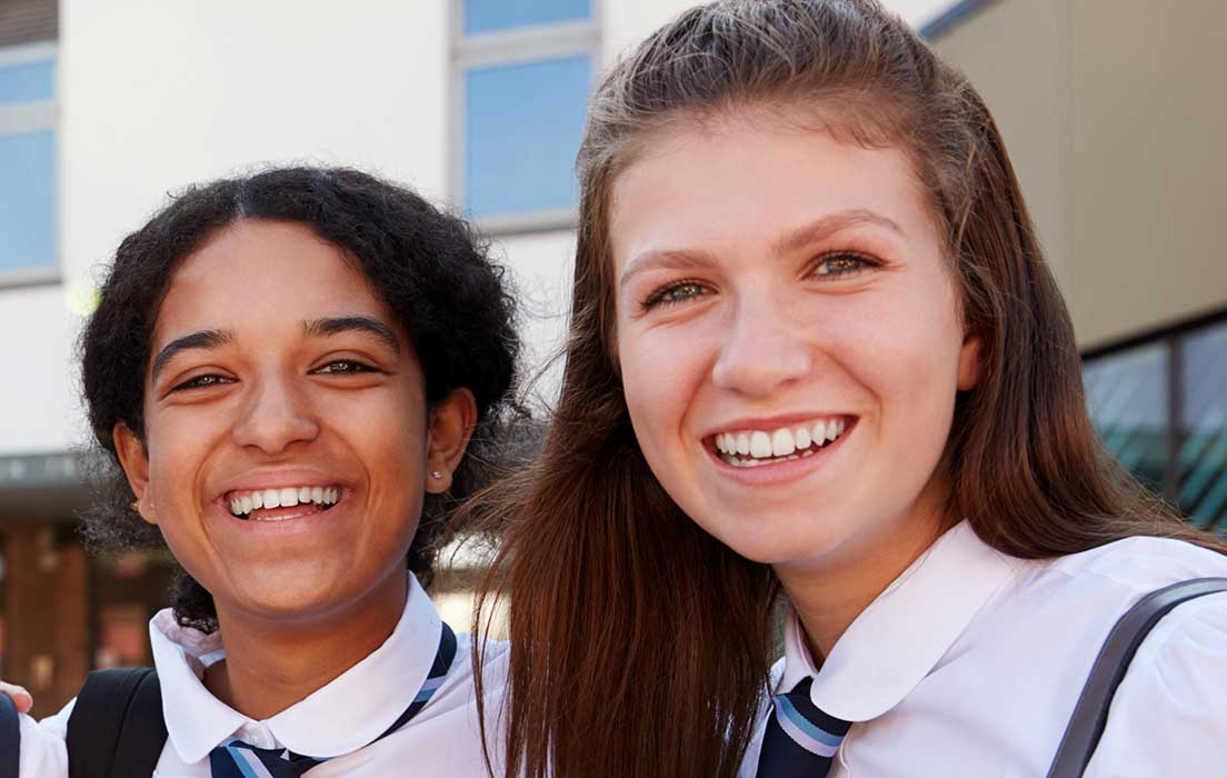 Two students wearing school uniform looking happy